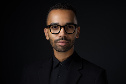 Professional headshot of a man wearing glasses and a black suit on a dark studio background by Montreal photographer Vadim Daniel