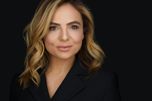 Professional headshot of a confident woman in black blazer with wavy blonde hair, photographed in Montreal on a dark background.